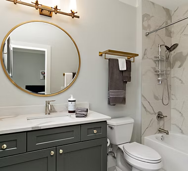 A home remodeling contractor working on a residential bathroom remodeling job — mid-task, hands, tools and the work itself in sharp focus, the rest of the space softly out of focus