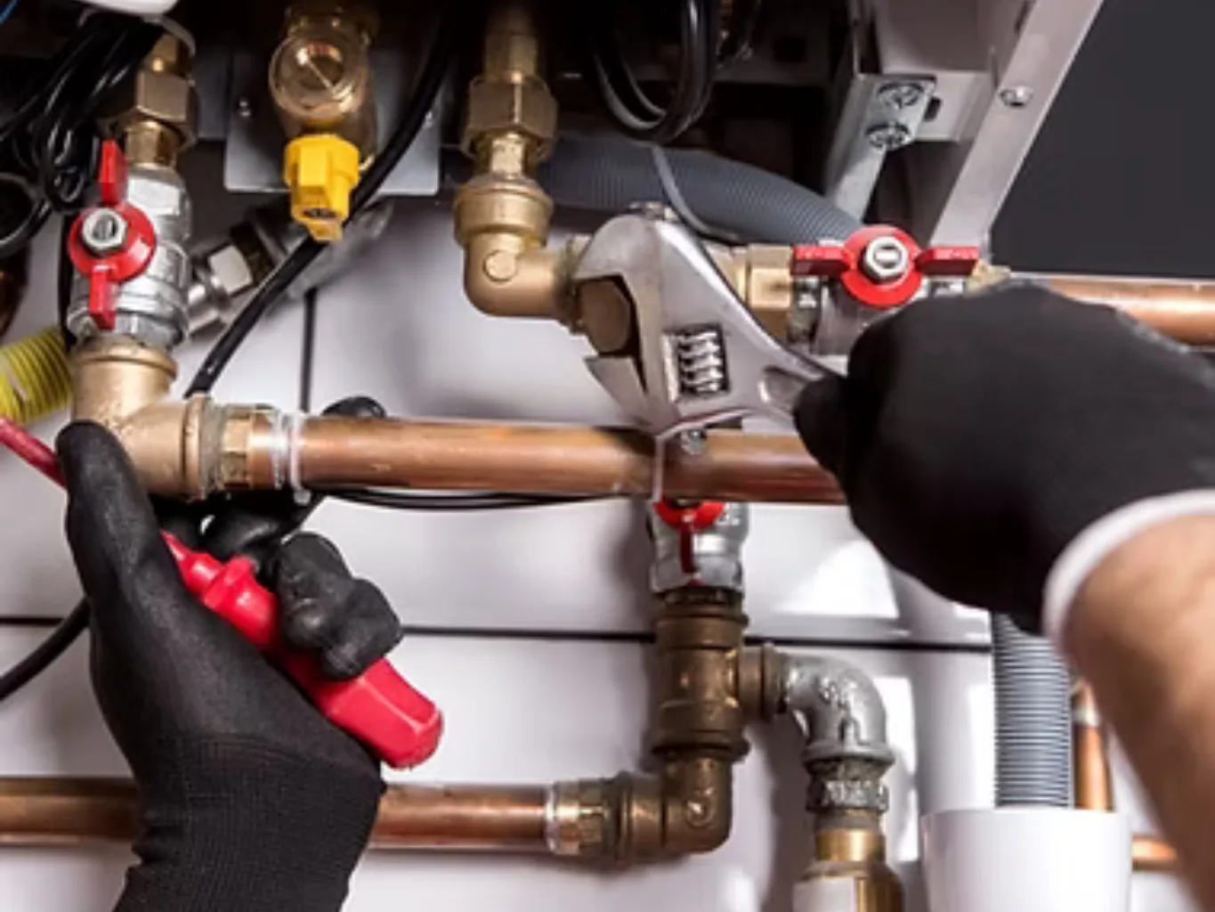 A home remodeling contractor working on a residential plumbing job — mid-task, hands, tools and the work itself in sharp focus, the rest of the space softly out of focus