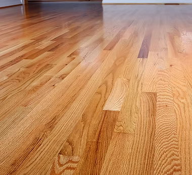 A home remodeling contractor working on a residential floor installation job — mid-task, hands, tools and the work itself in sharp focus, the rest of the space softly out of focus