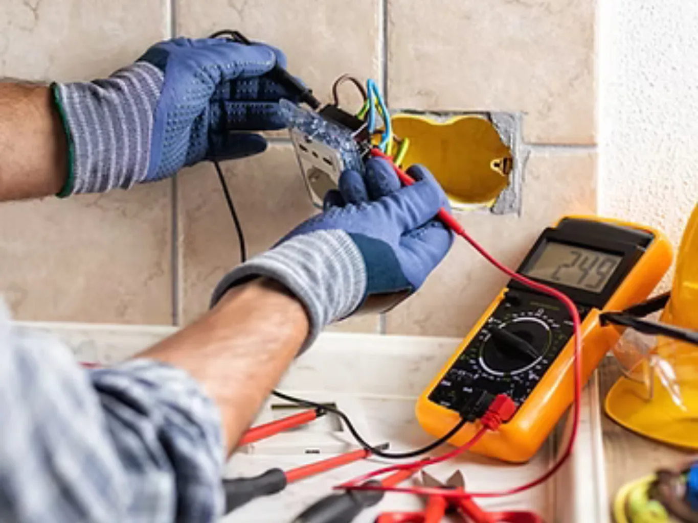 A home remodeling contractor working on a residential electrical job — mid-task, hands, tools and the work itself in sharp focus, the rest of the space softly out of focus