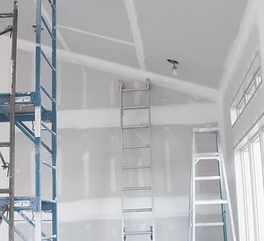 A home remodeling contractor working on a residential drywall job — mid-task, hands, tools and the work itself in sharp focus, the rest of the space softly out of focus
