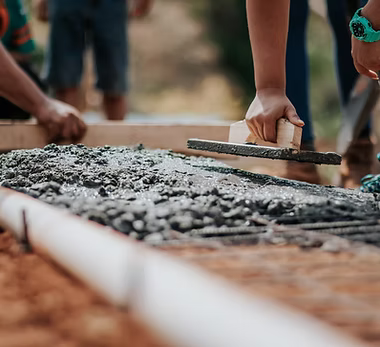 A home remodeling contractor working on a residential concrete and brick job — mid-task, hands, tools and the work itself in sharp focus, the rest of the space softly out of focus